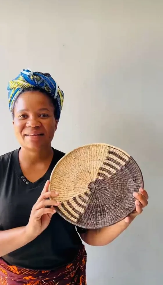 A weaver holding a large woven serving plate with a two-tone radial pattern