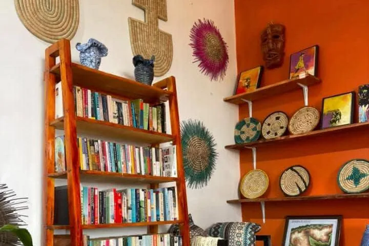 An art gallery interior in Malawi: coiled woven plates arranged on shelves against an orange wall, large woven wall pieces on the white wall, beside a bookcase