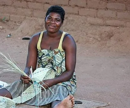 A weaver seated outdoors, coiling palm fibre into the base of a new basket