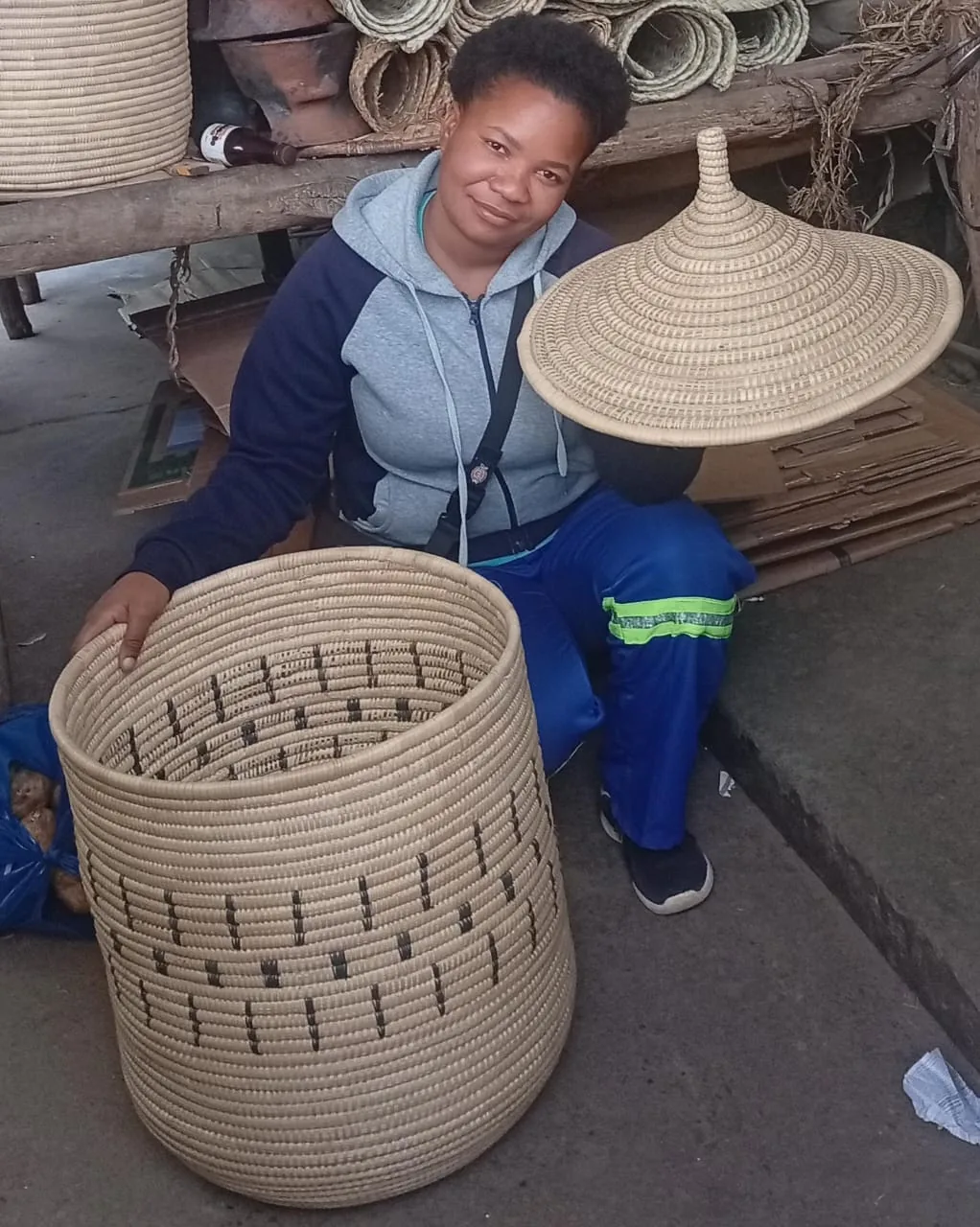 A weaver at the workshop holding a finished basket and a woven hat